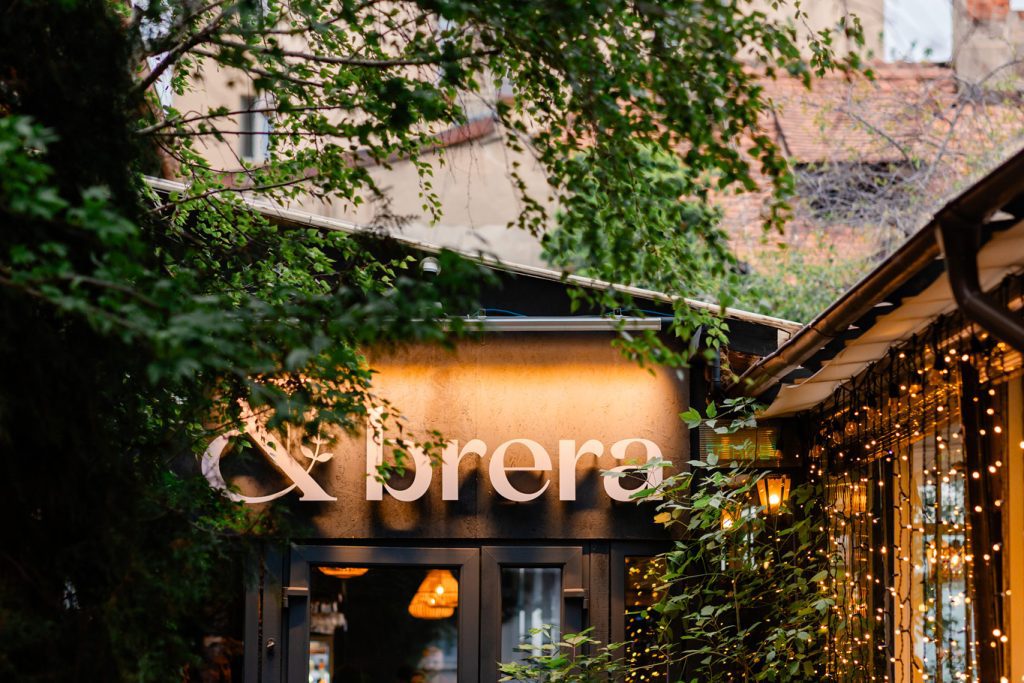 Intrarea Brera seara, cu firma luminată printre copaci