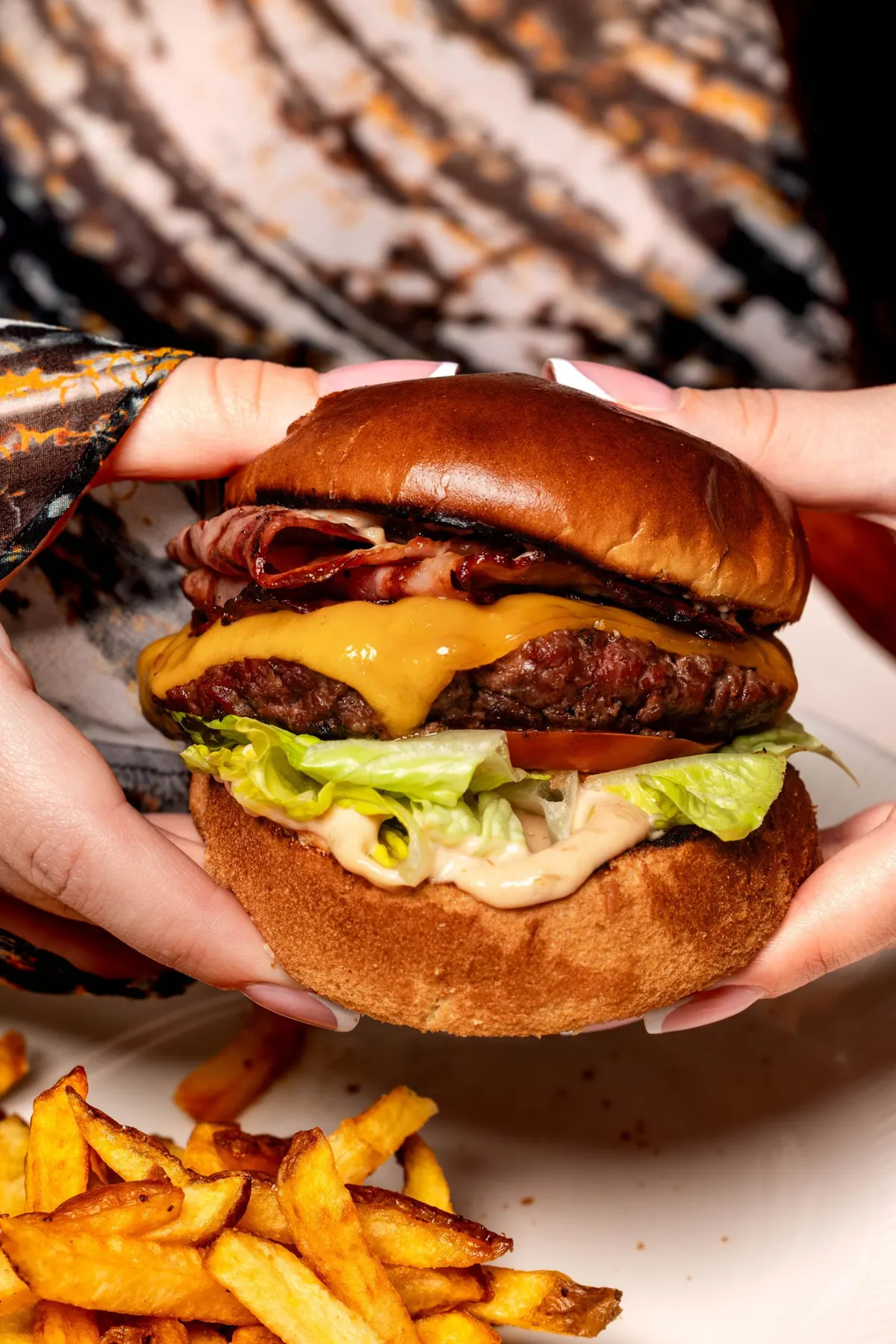 Burger cu cheddar și bacon, ținut în mâini, cu cartofi prăjiți