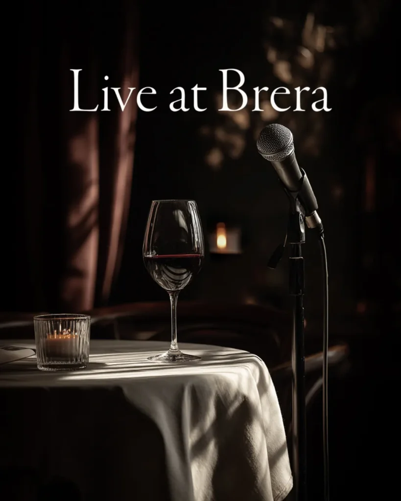 Afișul „Live at Brera”: un pahar de vin și un microfon pe o masă, în lumină caldă
