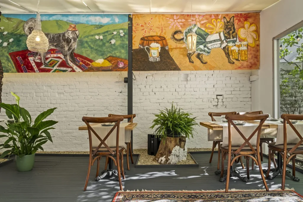 Sala cu pictura murală în stil naiv, mese de lemn și plante